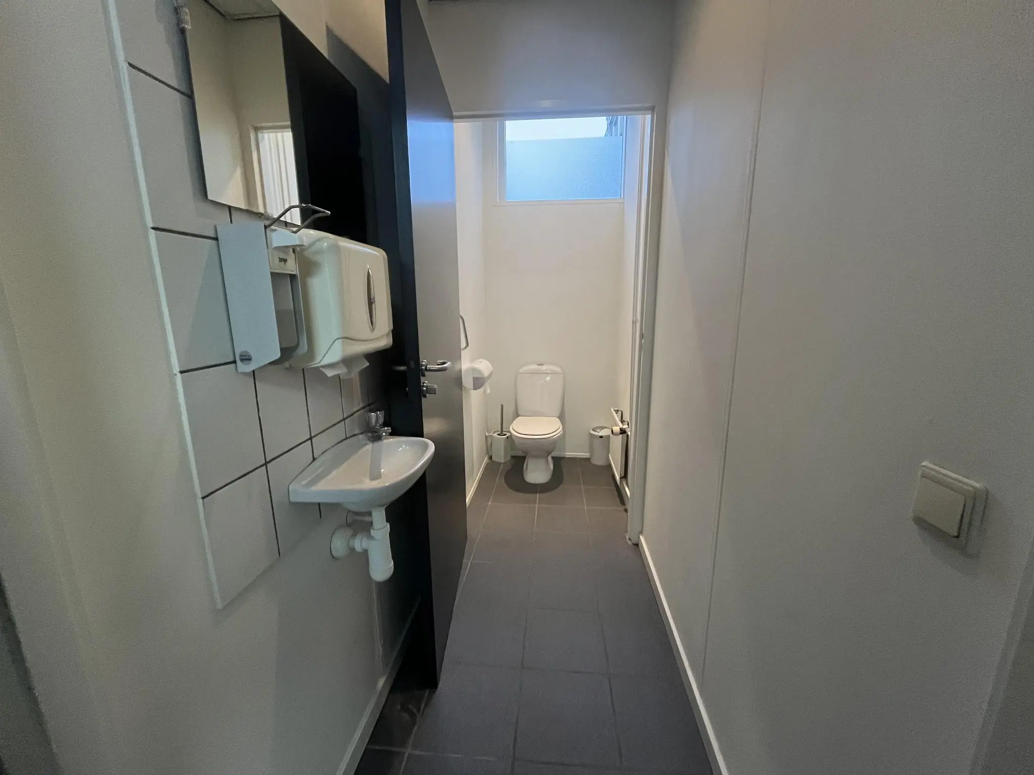 Smalle, betegelde toiletruimte aan de Burgemeester Smitsstraat met een toilet, wastafel en muurdispensers.